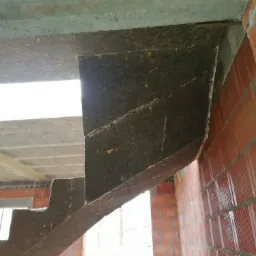 Surowe, betonowe schody w trakcie budowy, widoczne szalunki i fragment murowanej ściany z czerwonej cegły.