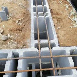 Wykonywanie szalunku traconego z bloczków betonowych zbrojonych stalą na fundamencie, widoczne wypełnienie szczelin pianką montażową.