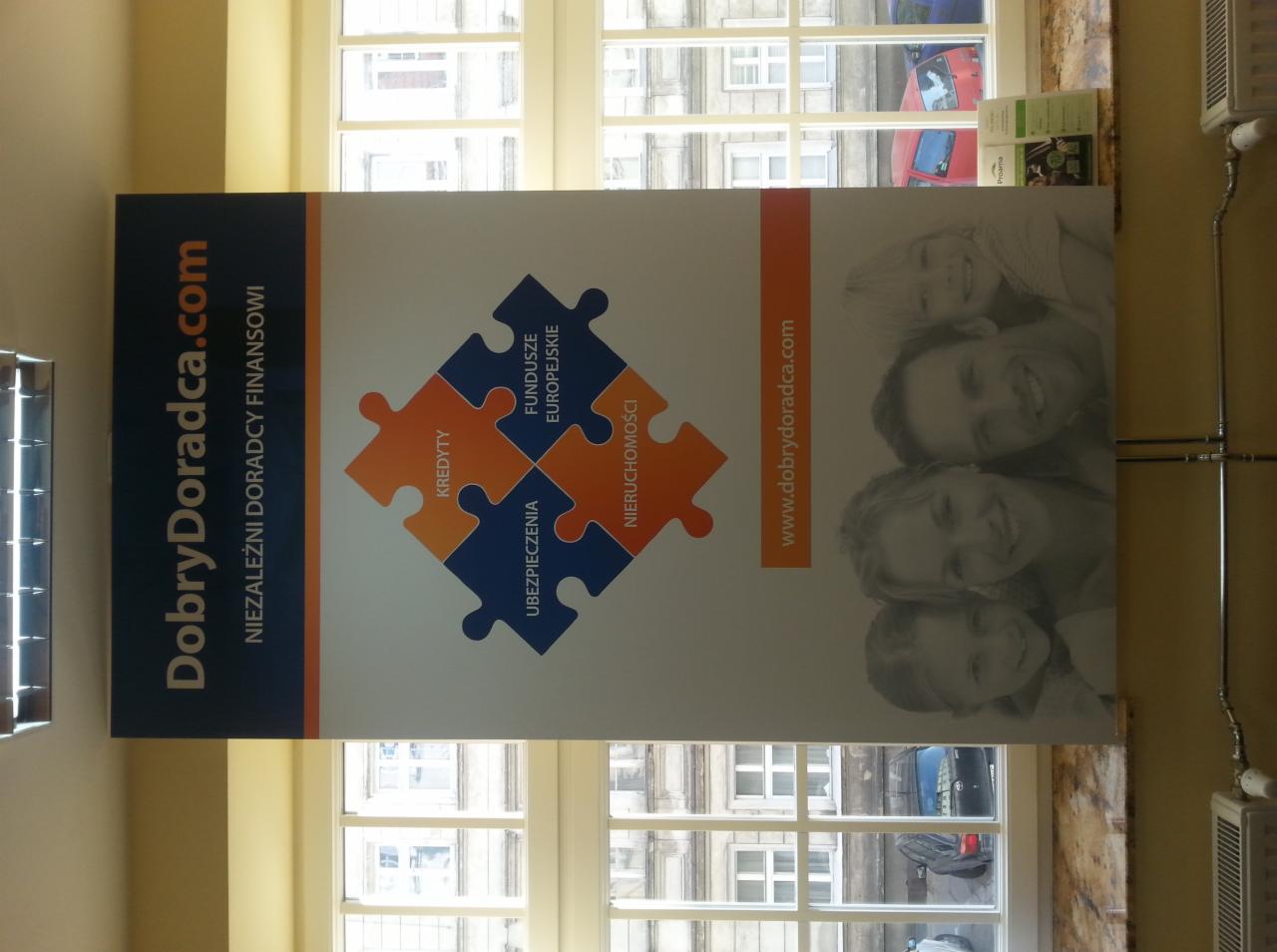 Baner reklamowy z logo firmy 'Dobry Doradca', oferującej niezależne doradztwo finansowe. Grafika z puzzli symbolizuje kredyty, ubezpieczenia i fundusze.