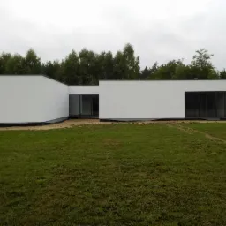 Nowoczesny, biały dom jednorodzinny z dużymi przeszkleniami na tle zielonego trawnika i drzew.