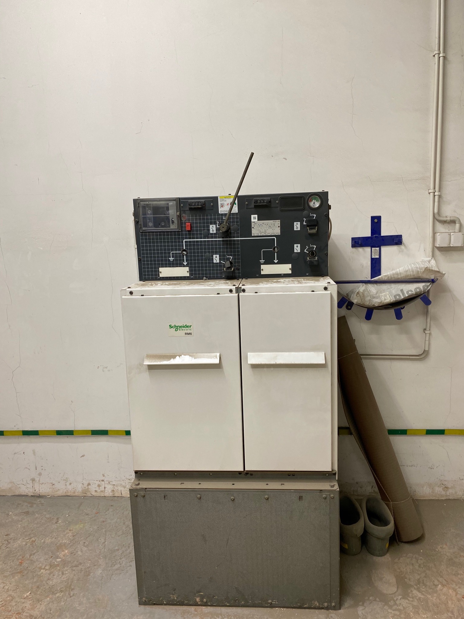 Rozdzielnia średniego napięcia Schneider Electric RM6, umieszczona w pomieszczeniu technicznym z widocznymi śladami użytkowania na ścianach i podłodze. Nad rozdzielnią panel sterowania...