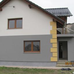 Zano - Ocieplony dom jednorodzinny z szarą elewacją, białym wykończeniem górnej części i dekoracyjnymi żółtymi elementami wokół wejścia, widok z zewnątrz.