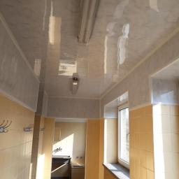 Zano - Wykończone wnętrze korytarza z marmurkową, błyszczącą okładziną sufitową i ścienną, żółte płytki na ścianach, widoczne wieszaki i okno z widokiem na zewnątrz.