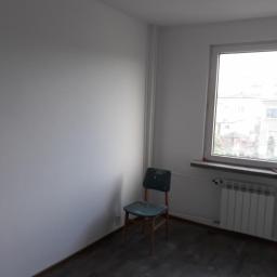 Zano - Wnętrze pokoju po remoncie: świeżo pomalowane białe ściany, ciemna podłoga, zielone krzesło przy ścianie, grzejnik pod oknem.