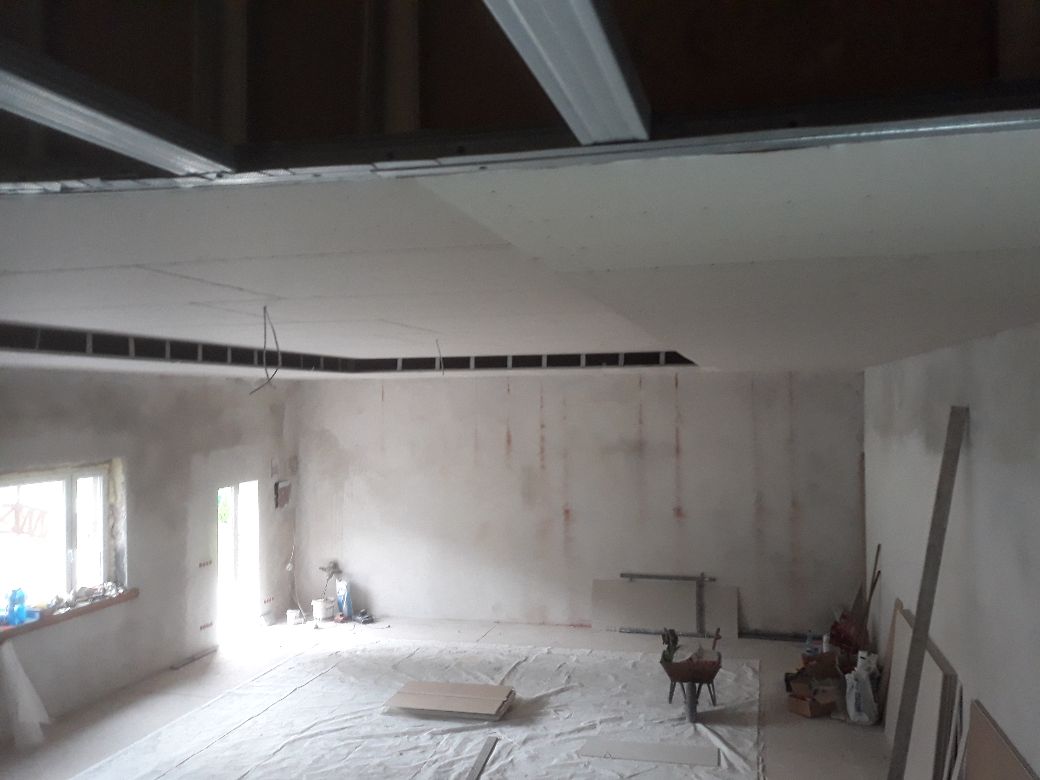 Wnętrze w trakcie montażu sufitu podwieszanego z płyty karton-gips, widoczne profile metalowe i częściowo zamontowane płyty, pomieszczenie zabezpieczone folią malarską.