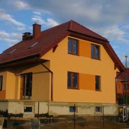 Domyszkieletowe24 - Nowo otynkowany dom jednorodzinny z czerwonym dachem, widoczne fragmenty fundamentów i przygotowany teren wokół budynku.