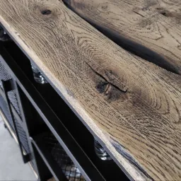 Metalowy regał z blatem z dwóch desek z wyraźnym usłojeniem i sękami, widoczne szklane butelki w przegródkach.