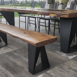 Firma Indust - Zestaw mebli ogrodowych: stół z blatem z litego drewna o nieregularnych krawędziach, wsparty na geometrycznych, metalowych nogach, oraz ławka o podobnej konstrukcji, uzupełniony o metalowe krzesła,...