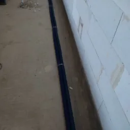 Dwa niebieskie peszle ułożone wzdłuż ściany z betonu komórkowego, widoczne fragmenty instalacji elektrycznej w trakcie prac wykończeniowych.