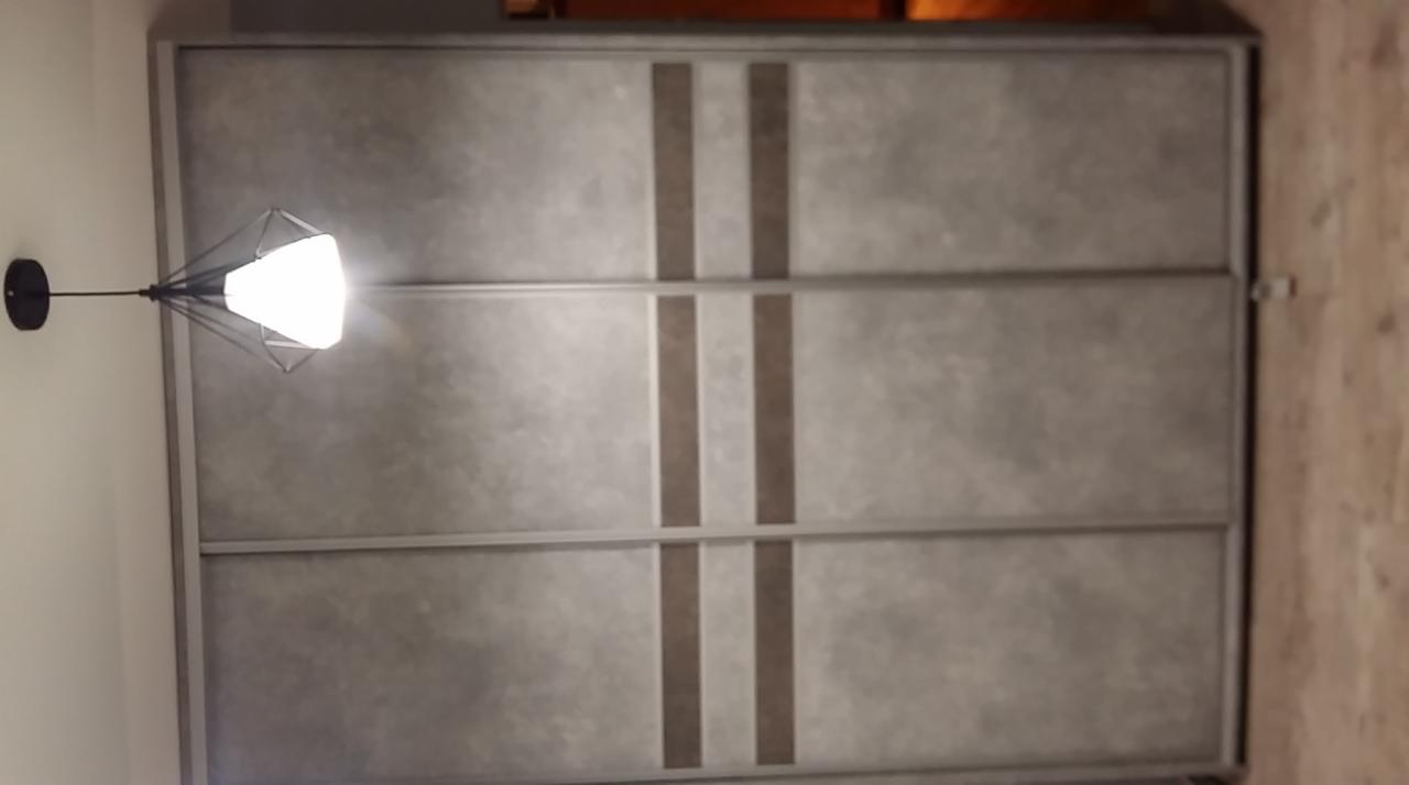 Szara szafa wnękowa z przesuwnymi drzwiami i pionowymi pasami, oświetlona nowoczesną lampą sufitową.