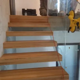 Montaż balustrady szklanej na drewnianych schodach przez dw&oacute;ch monter&oacute;w, widoczny uchwyt do szkła i skrzynka narzędziowa.