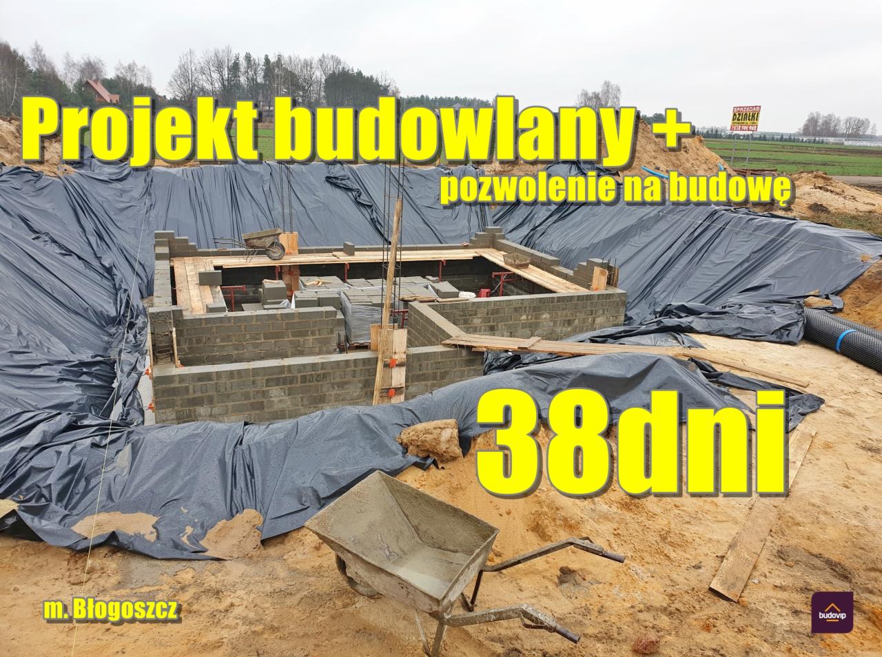 Fundamenty domu jednorodzinnego w trakcie budowy, zabezpieczone czarną folią, widoczna taczka z zaprawą, w tle krajobraz wiejski i tablica informacyjna o sprzedaży działek.