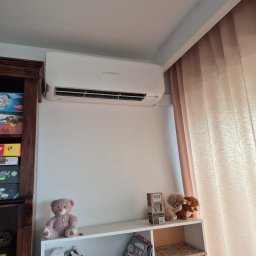 Klima-Premium Tomasz Bronowicz - Biały klimatyzator Mitsubishi na ścianie pokoju dziecięcego, obok regału z zabawkami i zasłony. Widok z dołu, oświetlenie dzienne.