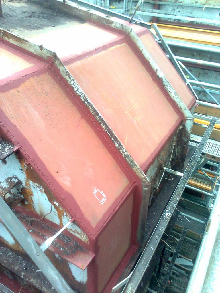 Szczegółowe ujęcie stalowej konstrukcji szalunkowej z widocznymi spawami i zabezpieczeniem antykorozyjnym w kolorze czerwonym, umieszczonej na rusztowaniu.