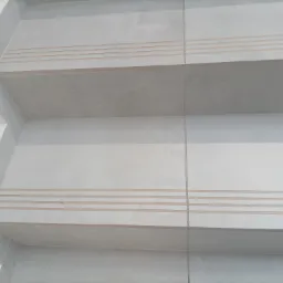 Jasnoszare płytki ceramiczne na schodach wewnętrznych z trzema poziomymi paskami antypoślizgowymi na krawędziach stopni.