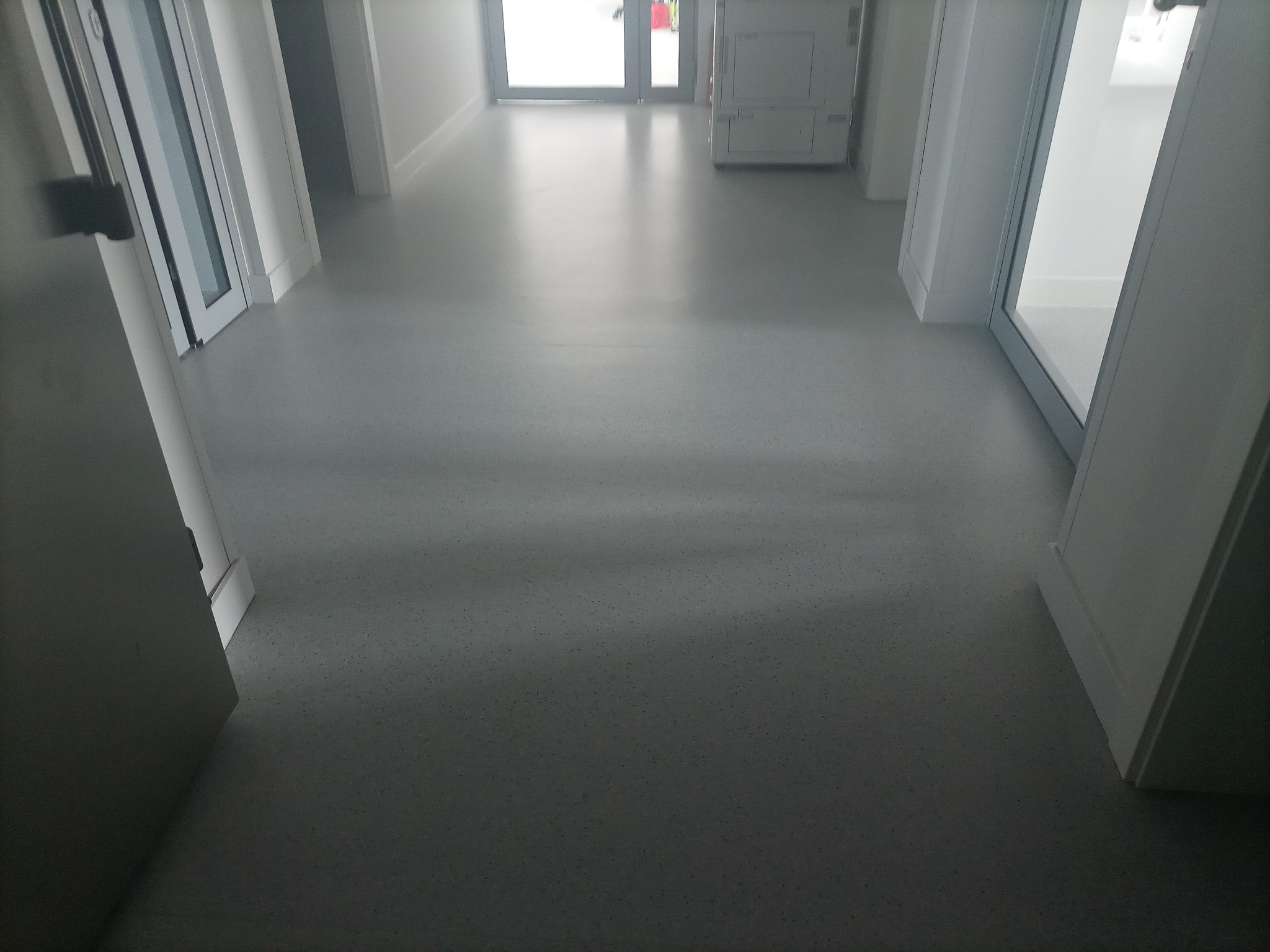 Szary korytarz biurowy z gładką podłogą, białymi ścianami i drzwiami, widok z niskiej perspektywy.