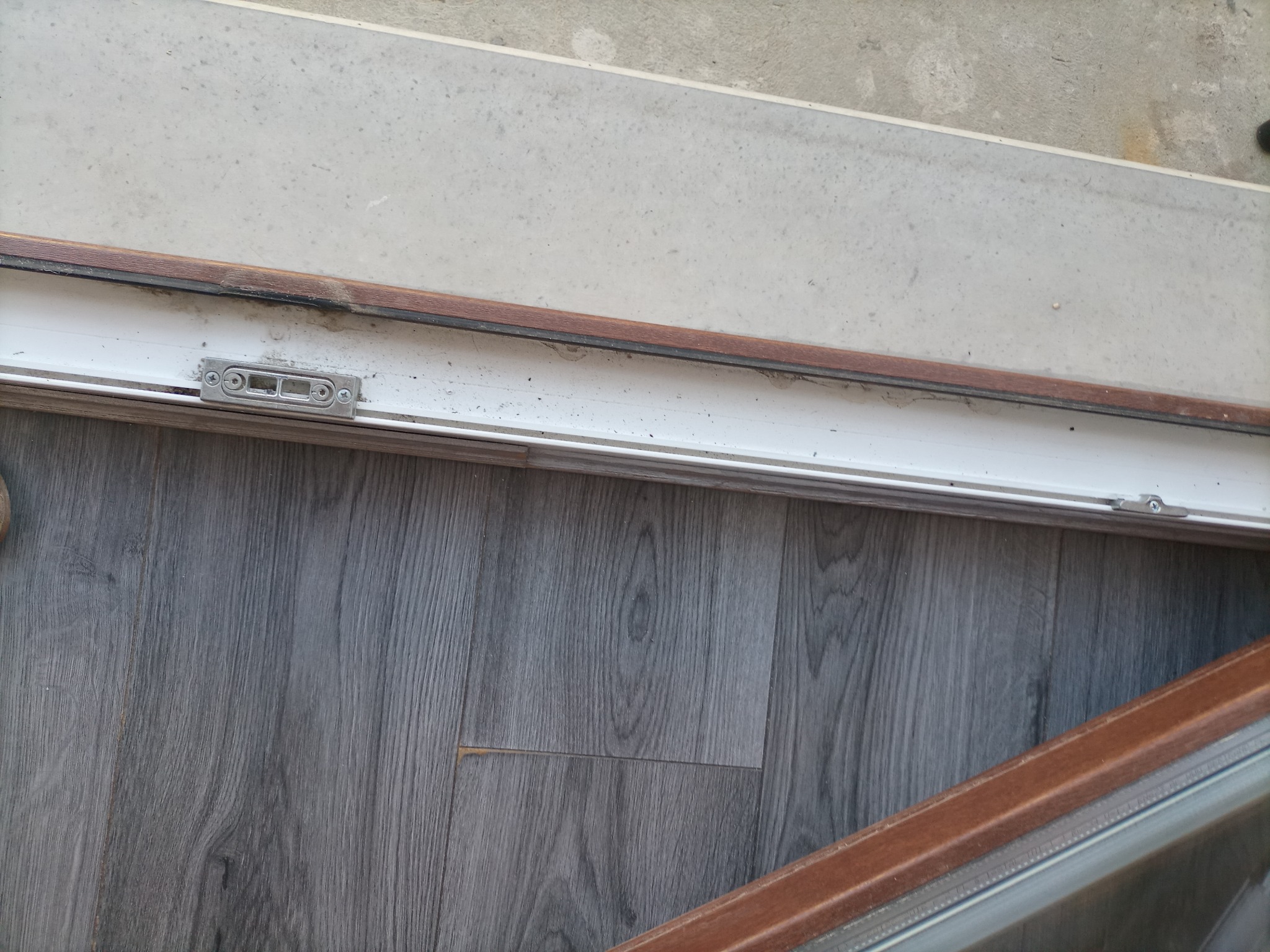 Szczegółowe ujęcie okna PCV z widocznym brudem i kurzem w prowadnicach i na uszczelkach, ukazujące potrzebę dokładnego mycia okien.