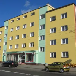 Żółty, wielopiętrowy budynek po renowacji z reklamami Rossmann i Bar Kebab na bocznej ścianie, widoczne samochody i chodnik.