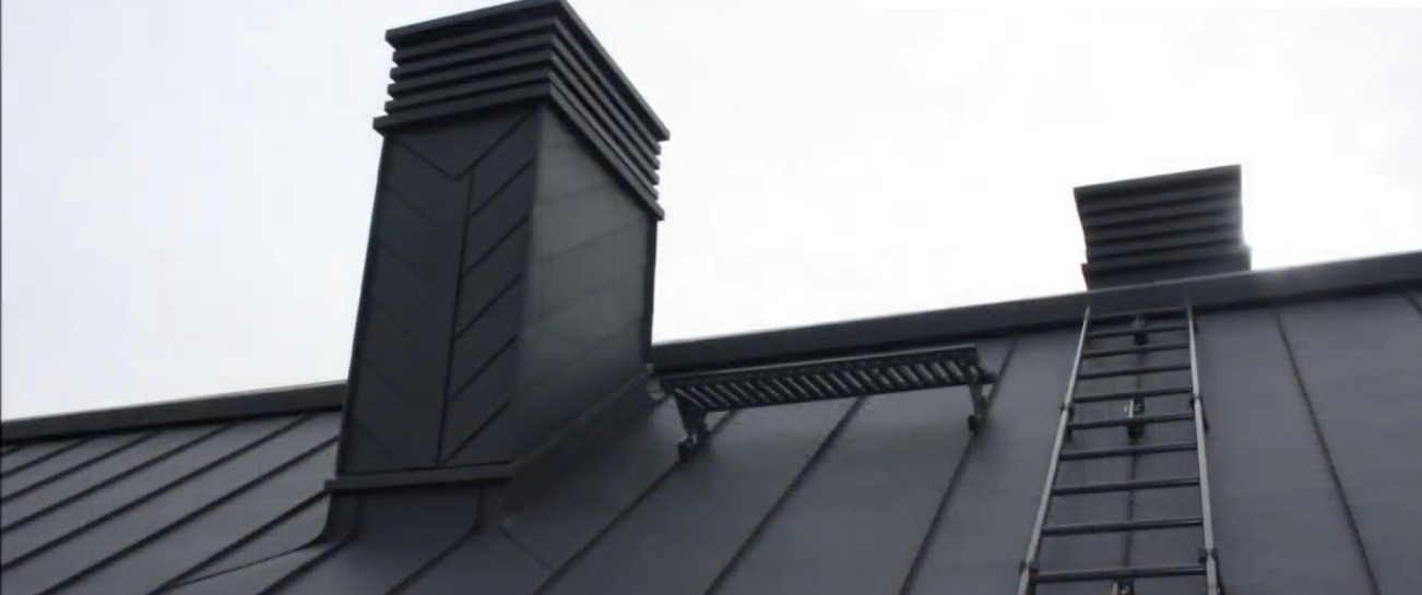 Grafitowy dach z blachy na rąbek stojący z dwoma kominami w nowoczesnym stylu i drabina dekarska.