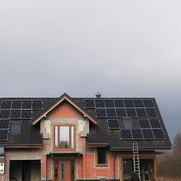 Ekopompaciepła.pl Sp. z o.o. - Dom w trakcie budowy z zamontowanymi panelami fotowoltaicznymi na dachu pokrytym ciemną dachówką, widoczna drabina oparta o ścianę budynku.