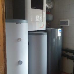 Ekopompaciepła.pl Sp. z o.o. - Zestaw urządzeń grzewczych w kotłowni: dwa białe zasobniki Nibe z szarymi akcentami, centrala wentylacyjna Zehnder Comfo Q z czarnym panelem, oraz srebrne rury wentylacyjne pod sufitem, na tle...