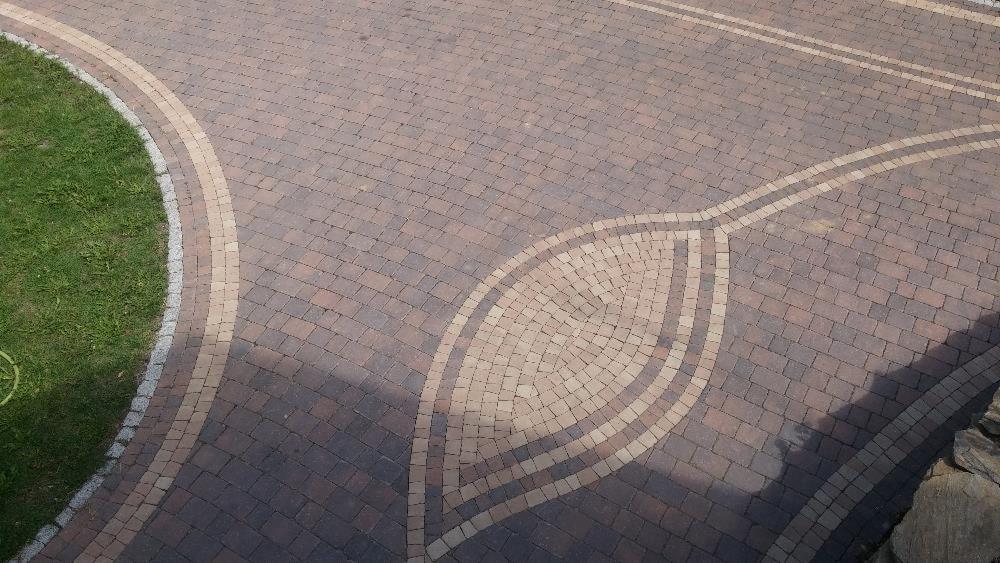 Wzór z kostki brukowej w kształcie liścia, obrzeża z jaśniejszych kostek, trawnik po lewej stronie, widok z góry.
