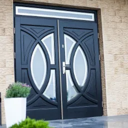 Eleganckie, podwójne, czarne skrzydła z owalnymi przeszkleniami, umieszczone w fasadzie budynku z dekoracyjną, jasną cegłą, z widoczną lampą ścienną i dwoma metalowymi koszami na śmieci...