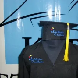 Czarna toga i biret absolwenckie z wyhaftowanym logo 'lyceum oudshoorn' na tle plakatu.