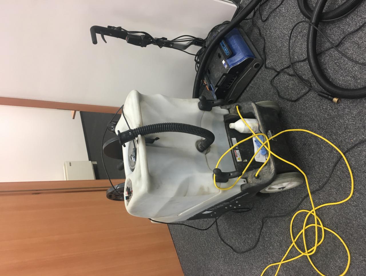 Profesjonalna maszyna do czyszczenia dywanów i wykładzin w biurze, z widocznymi przewodami i pojemnikiem na detergent.