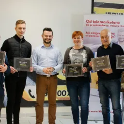 Grupa sześciu osób, w tym jedna kobieta, prezentuje certyfikaty ukończenia szkolenia DEAL MAKER PRO, stojąc na tle grafiki reklamowej z hasłem 'Od telemarketera do przedsiębiorcy, mówcy i trenera'.