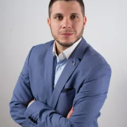 Portret mężczyzny w błękitnym garniturze na jasnym tle, z rękami skrzyżowanymi na piersiach, reprezentujący profesjonalizm firmy z Gliwic.