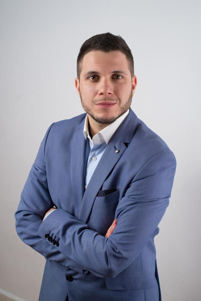 Portret mężczyzny w błękitnym garniturze na jasnym tle, z rękami skrzyżowanymi na piersiach, reprezentujący profesjonalizm firmy z Gliwic.