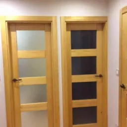 Dwa drewniane drzwi wewnętrzne z trzema przeszkleniami, jeden z matowym szkłem, drugi z ciemnym, widok na fragment trzecich drzwi.