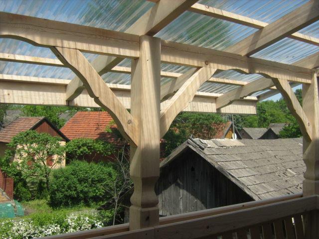 Drewniana konstrukcja z przezroczystym zadaszeniem, widok z dołu na tle zabudowań wiejskich i zieleni.