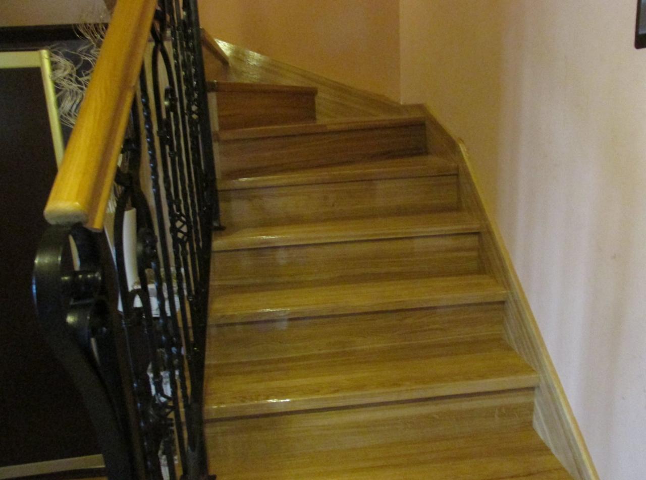 Drewniane schody z metalową, zdobioną balustradą i drewnianą poręczą, prowadzące do góry, widok z dołu.