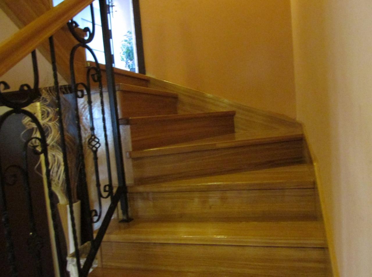 Zakręcone schody z jasnego drewna z czarną, kutą balustradą, oświetlone padającym światłem dziennym z okna w tle.