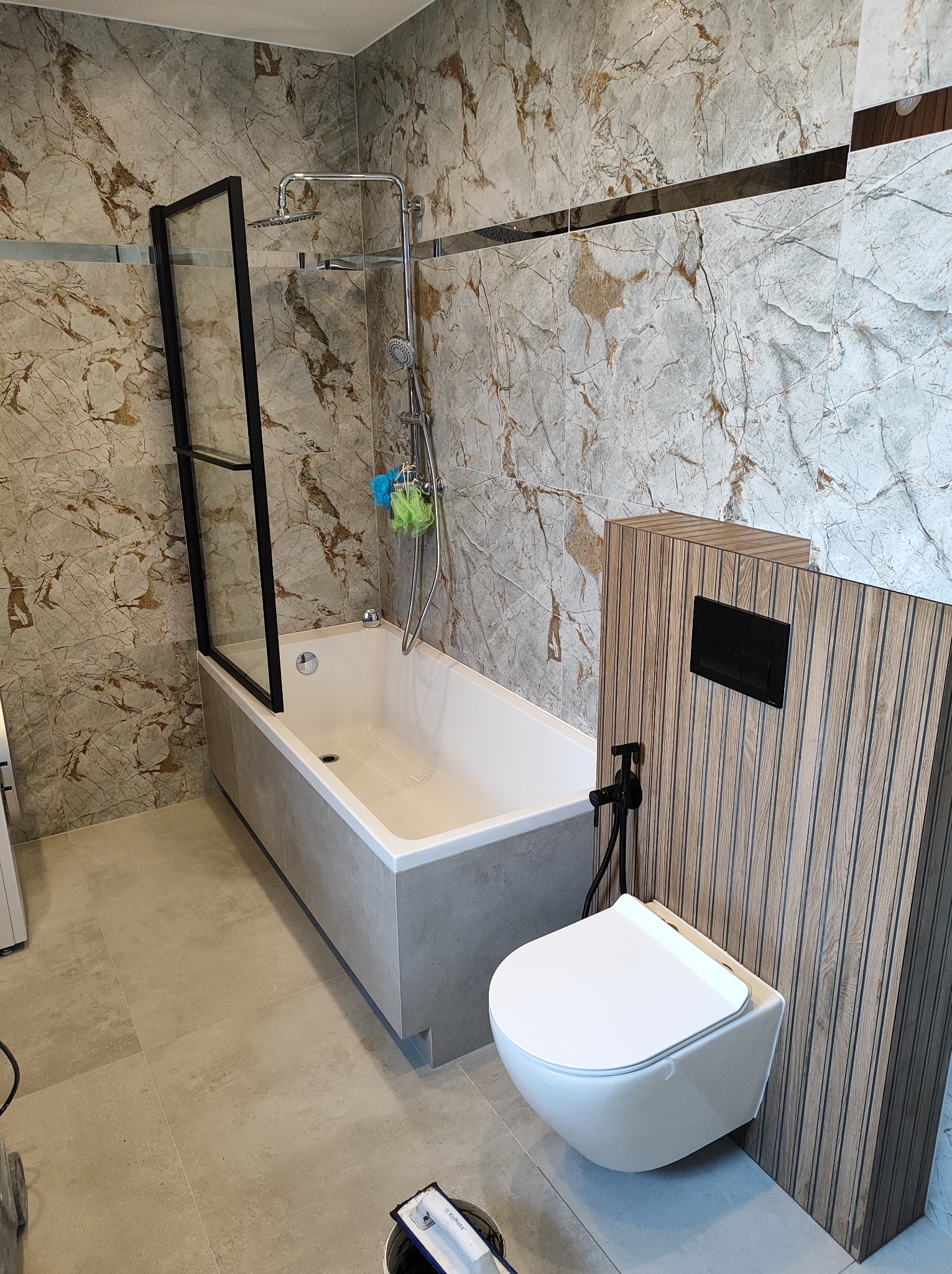 Nowoczesna łazienka z wanną z czarną ramą prysznicową, podwieszaną toaletą z czarną armaturą i płytkami imitującymi marmur na ścianach.