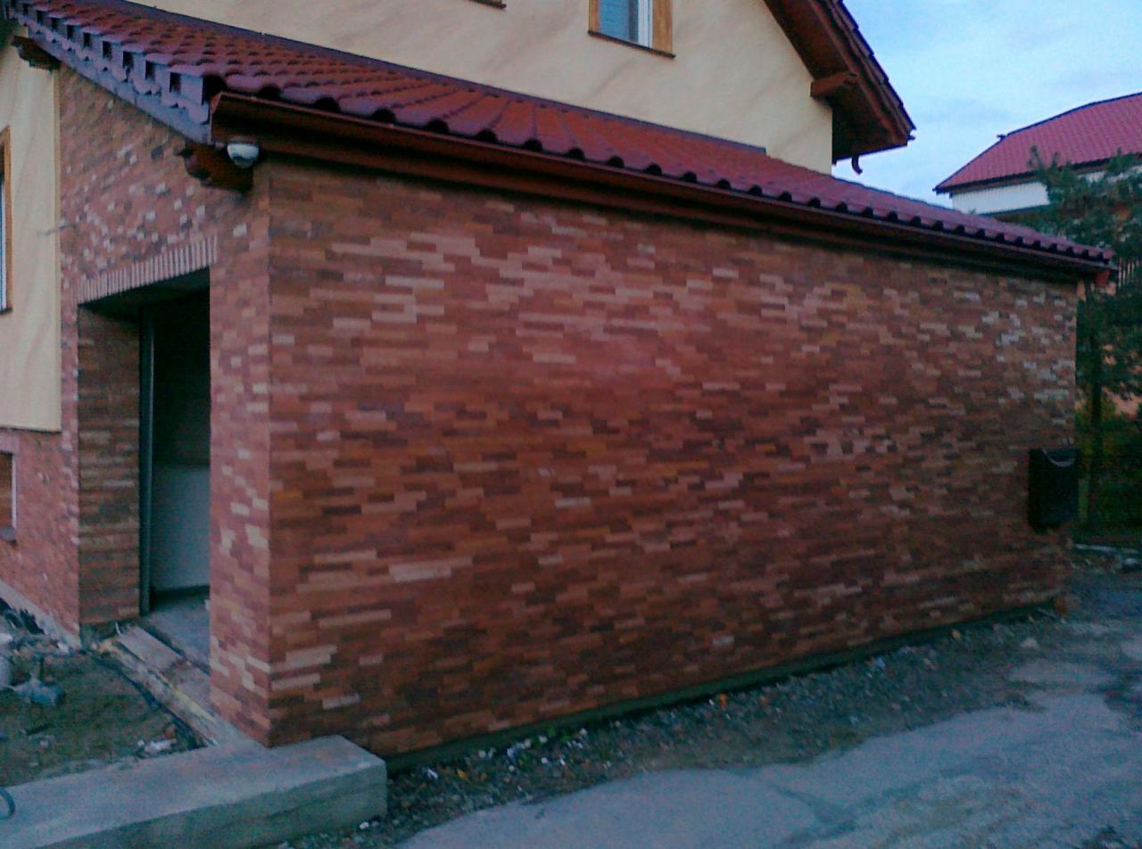 Nowo wybudowany, ceglany garaż przylegający do domu, z widocznym wejściem i fragmentami kostki brukowej na podjeździe.