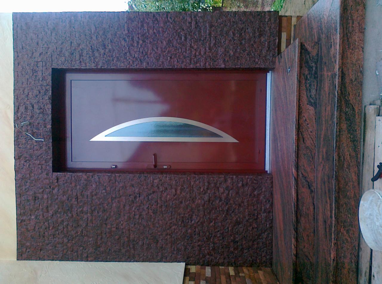 Brązowe okno z półokrągłym przeszkleniem osadzone w ścianie wykończonej drobną, brązową mozaiką kamienną, obok widoczny fragment ściany z płyty imitującej marmur.