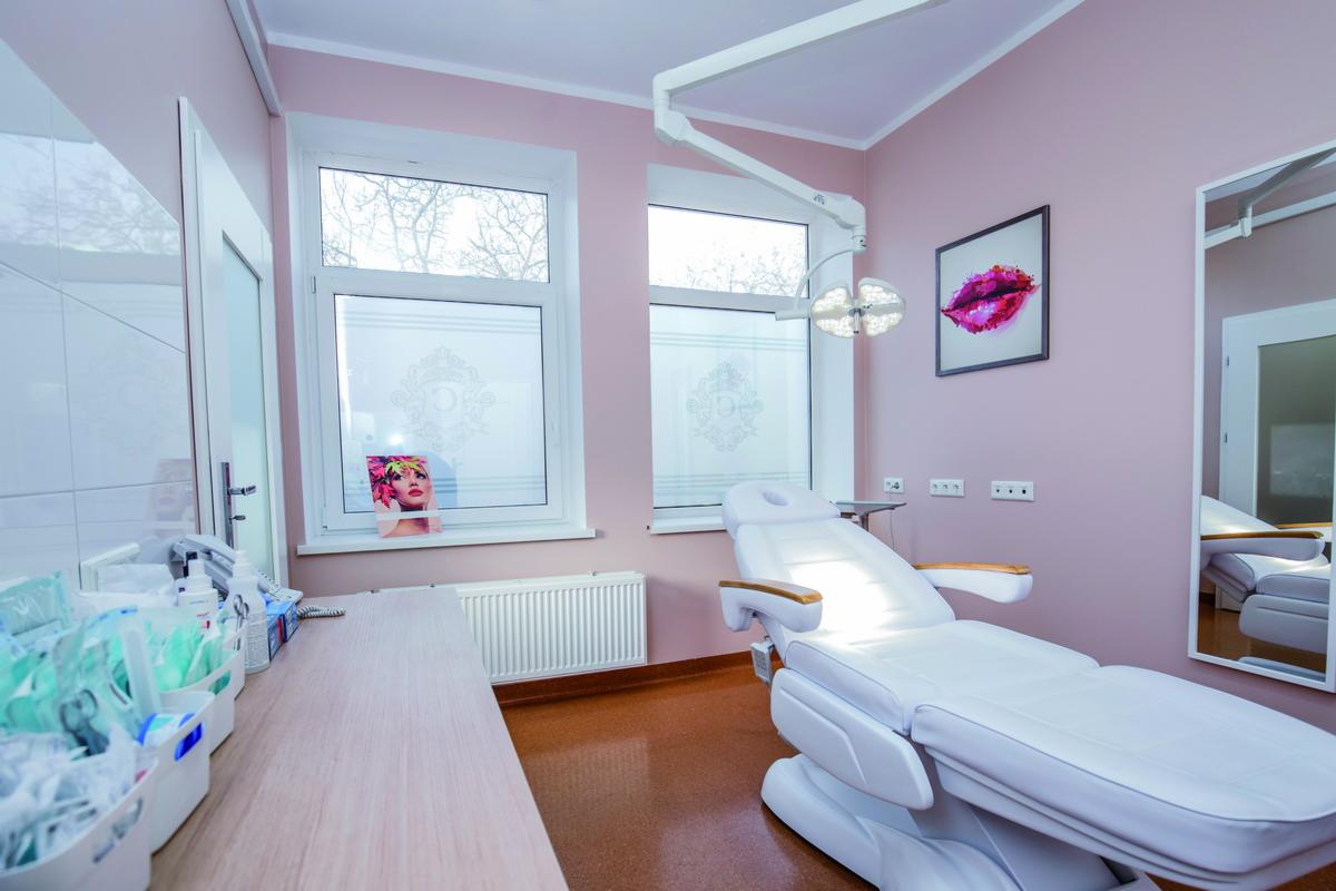 Jasny gabinet z białym, regulowanym fotelem zabiegowym, lampą medyczną i dekoracjami w odcieniach różu.