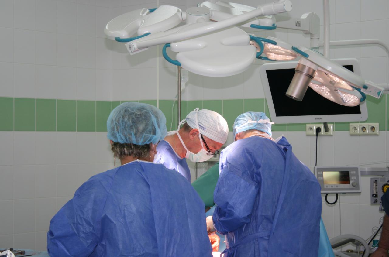 Zespół lekarzy w strojach ochronnych podczas operacji, widoczny monitor i lampa operacyjna.