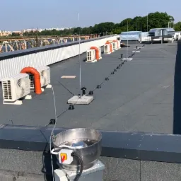 Widok z góry na instalację wentylacyjną i klimatyzacyjną na dachu budynku komercyjnego, z widocznymi jednostkami zewnętrznymi klimatyzatorów, kominami wentylacyjnymi, systemem odgromowym...