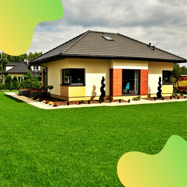 Nowoczesny parterowy dom z kremową elewacją, ciemną dachówką i ceglanym akcentem przy oknie, otoczony zielonym trawnikiem i ozdobnymi krzewami.