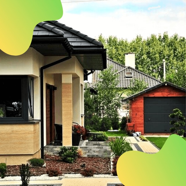 Nowoczesny dom jednorodzinny z ciemną dachówką i jasną elewacją, widok na wejście z kolumnami i zadbany ogród z kostką brukową oraz garaż wolnostojący w tle.