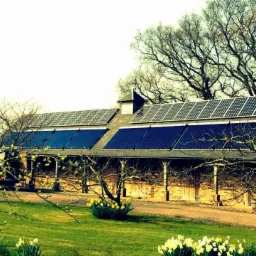 Rustykalny budynek gospodarczy z panelami słonecznymi i kolektorami słonecznymi na dachu, otoczony wiosenną zielenią i kwitnącymi narcyzami.