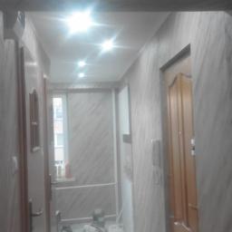 Rafał Bulo - Korytarz w trakcie malowania z widocznymi wiaderkami z farbą, zabezpieczoną folią podłogą i świeżo pomalowanymi ścianami imitującymi marmur.