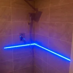 Nowoczesna kabina prysznicowa wyłożona szarymi płytkami z podświetleniem LED w kolorze niebieskim biegnącym wzdłuż ściany.