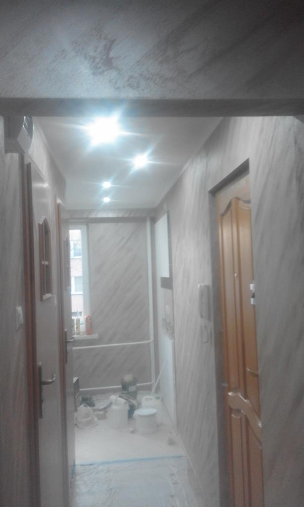 Korytarz w trakcie malowania z widocznymi wiaderkami z farbą, zabezpieczoną folią podłogą i świeżo pomalowanymi ścianami imitującymi marmur.