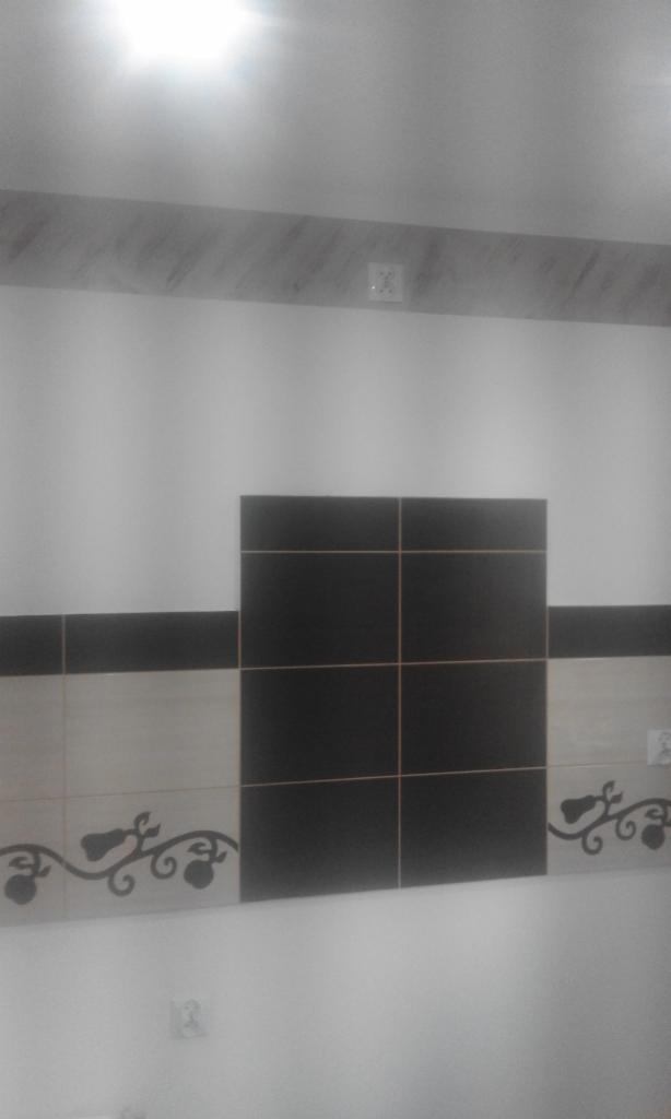 Fragment ściany w łazience z ułożonymi płytkami w kolorach czerni i beżu, z dekoracyjnym motywem roślinnym, widoczne gniazdko elektryczne