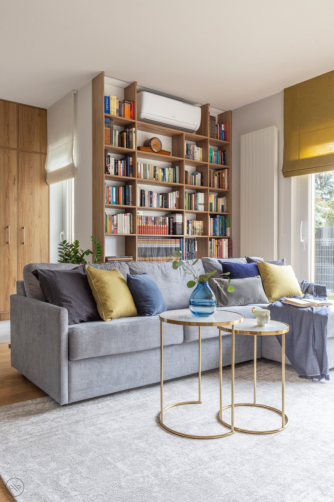 Jasny salon z szarą sofą, marmurowymi stolikami kawowymi na złotych nóżkach, regałem z książkami i klimatyzacją na górze w domu w Warszawie.